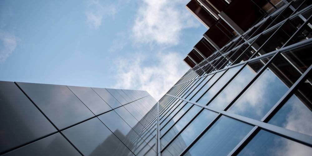 Hoog shot van een modern gebouw (provinciehuis Overijssel) met glazen gevel tegen een blauwe lucht.