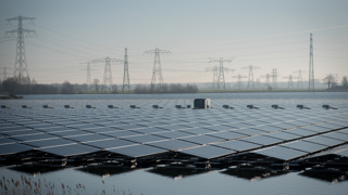 Groot veld met zonnepanelen boven het water met op de achtergrond hoogspanningsmasten