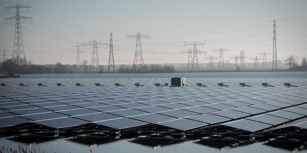 Groot veld met zonnepanelen boven het water met op de achtergrond hoogspanningsmasten