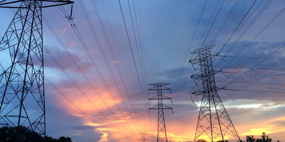 Hoogspanningsmasten met een blauwe wolkenlucht en oranje verkleuring door het zonlicht