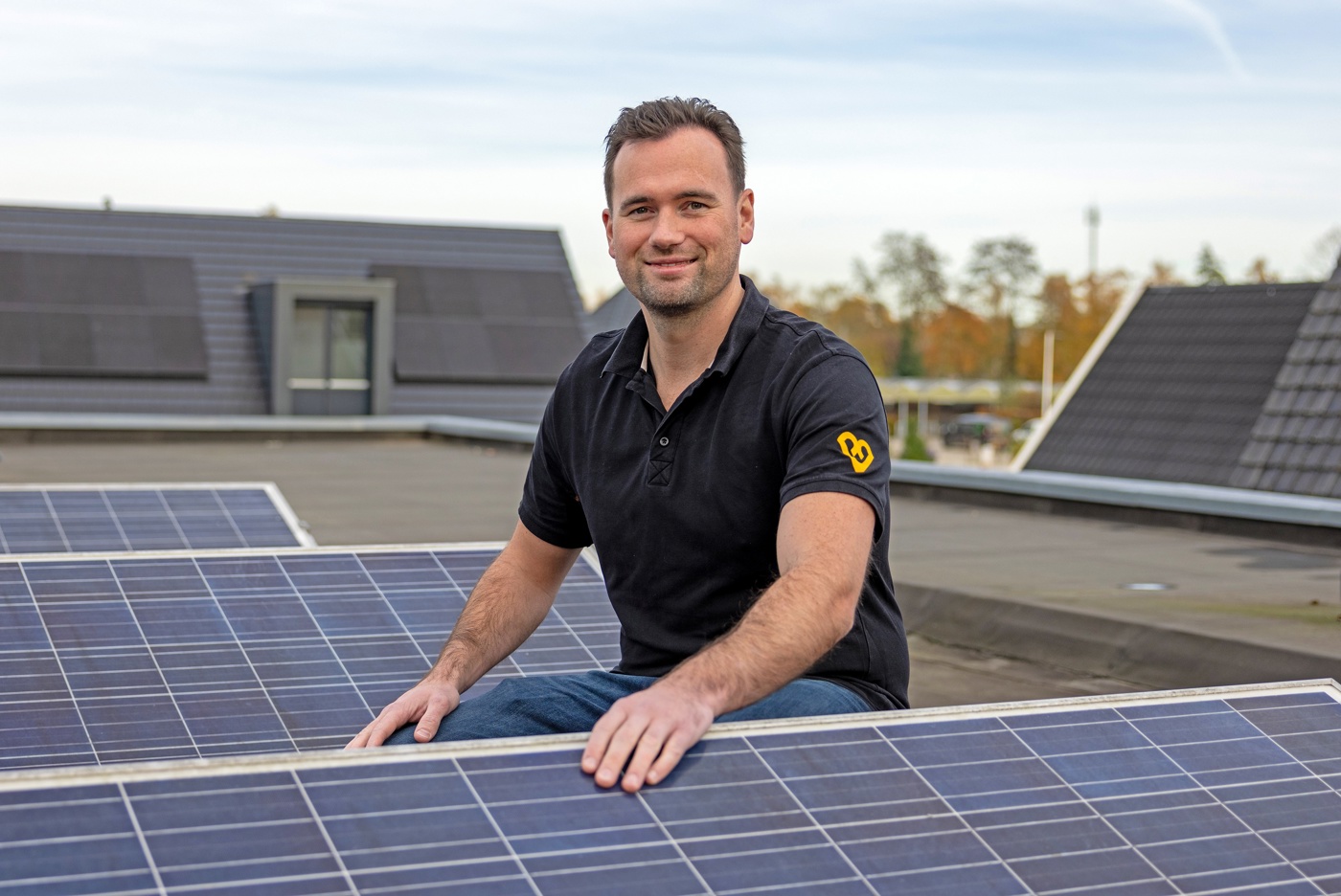 Mark buiten op het  dak van het bedrijf. Hij zit gehurkt bij de zonnepanelen.