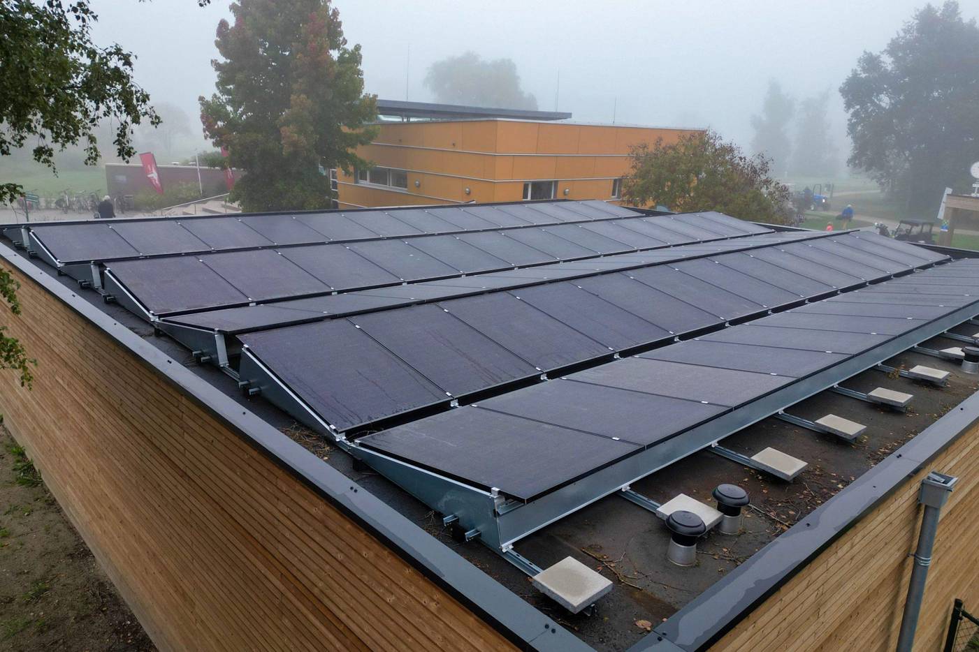 Een groot aantal zonnepanelen op een houten gebouw, omgeven door een mistig landschap.