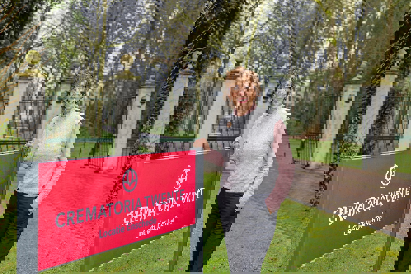 Harriet Tomassen, directeur-bestuurder van Crematoria Twente, buiten bij een bord van de crematoria. Op het bord staat de tekst: Crematoria Twente, locatie Enschede.