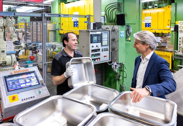 Wim ter Steege praat op de werkvloer met een medewerker van Reginox die nieuwe rvs spoelbakken netjes stapelt met werkhandschoenen aan.