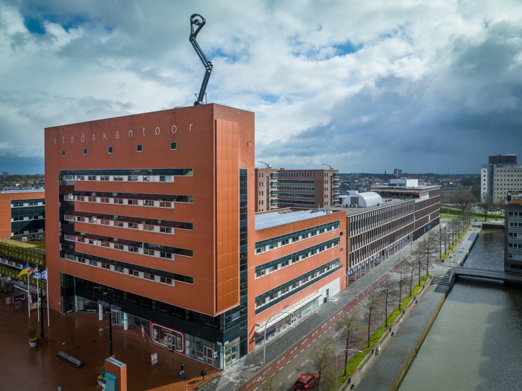 Stadskantoor in Zwolle met kunstwerk op het dak en zonnepanelen op de gevel. Op de gevel staat ook de naam 'Stadskantoor'.