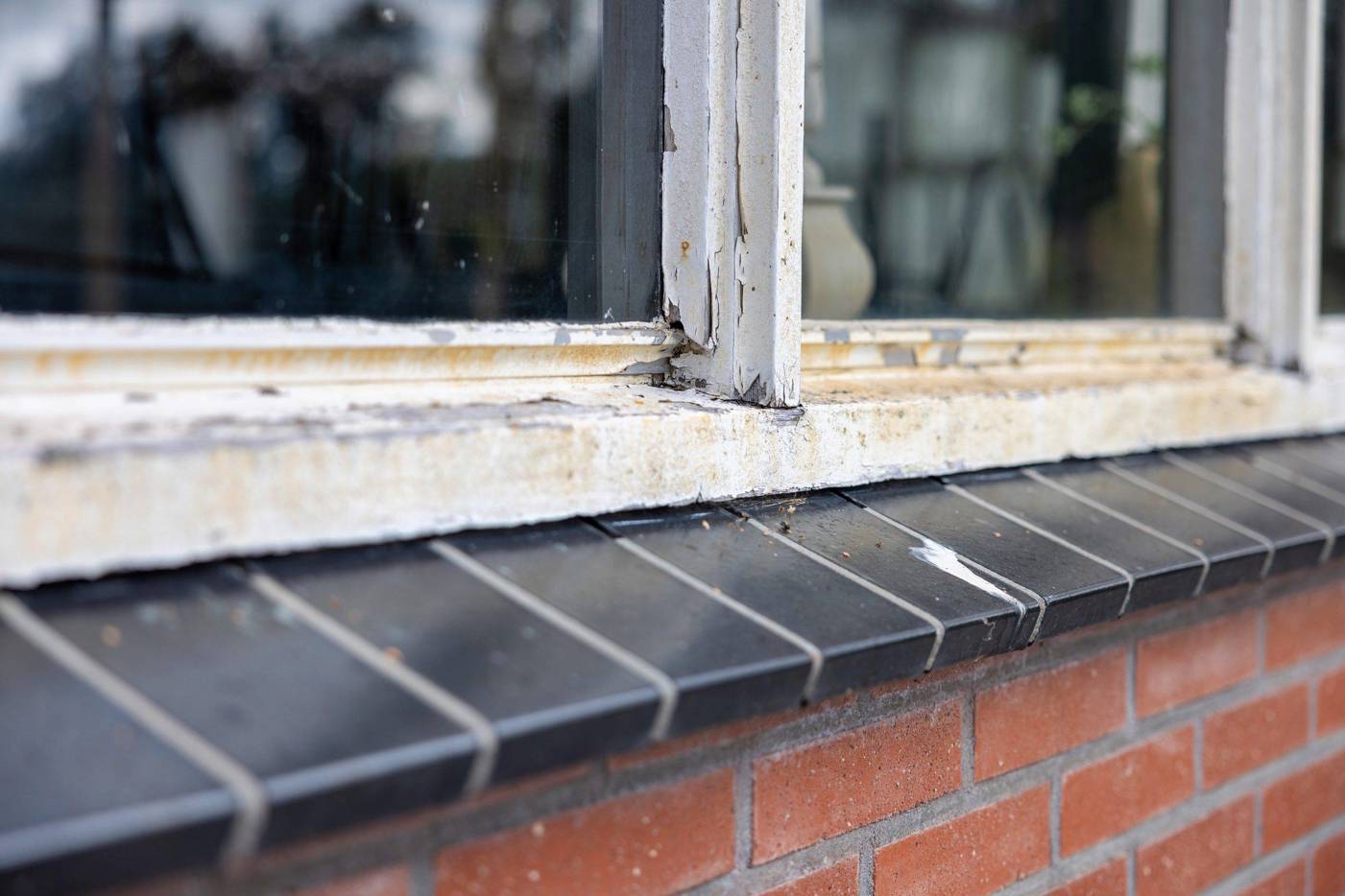 Close‑up van een oud en beschadigd houten raamkozijn met afgebladderde verf en zichtbare slijtage.