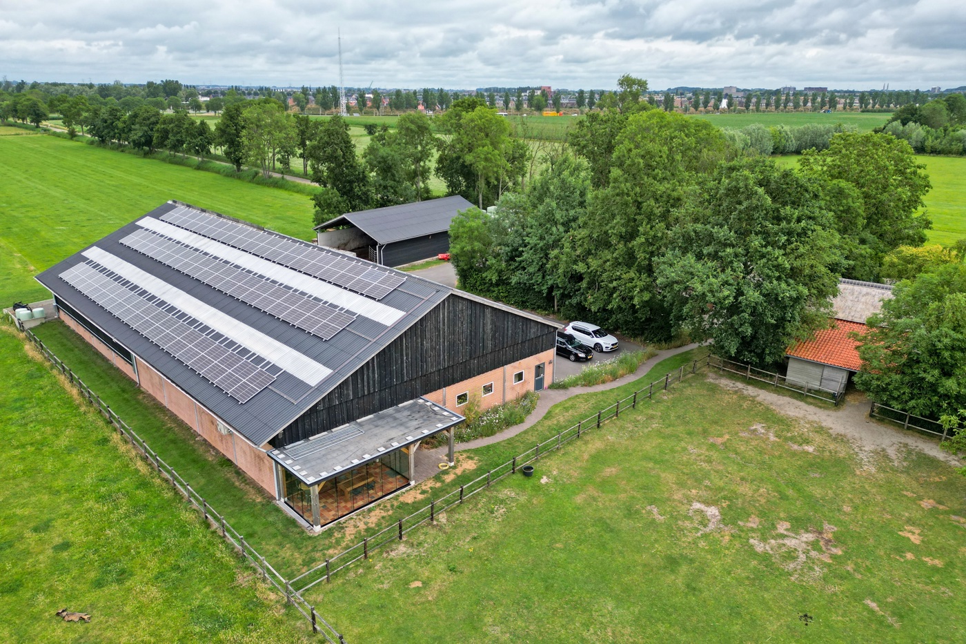 Grote boerenschuur met 3 rijen zonnepanelen op het dak. Omgeven door weilanden en 2 kleinere agrarische gebouwen.