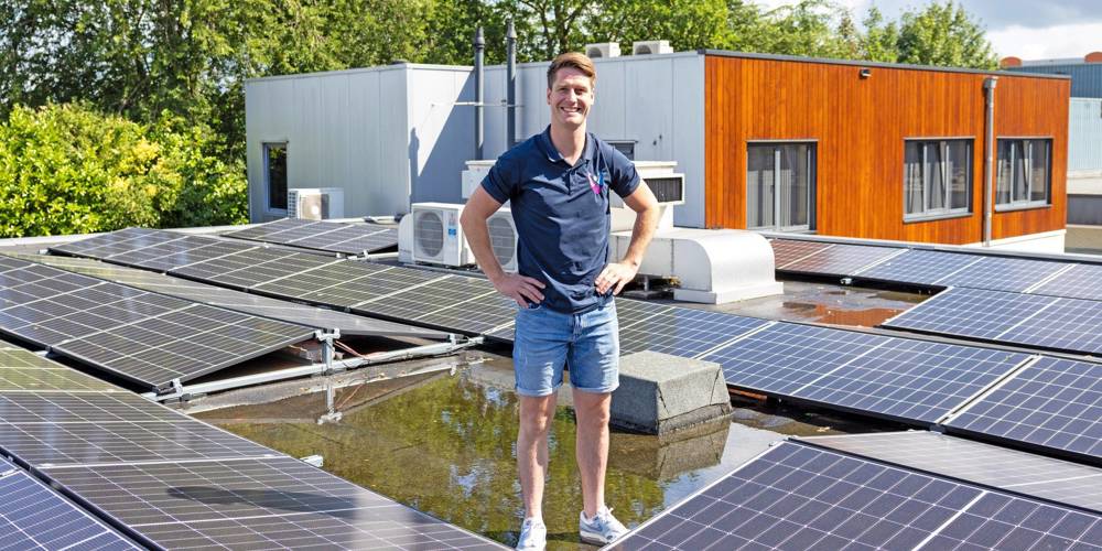 Tim Waaijer staat op een dak tussen meerdere zonnepanelen, met gebouwen en bomen op de achtergrond.